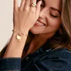 A woman wearing a denim jacket and jewelry, smiling. Produktbild-Vorschau