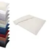 A stack of folded bedding in various colors is shown on the left, with a single cream-colored duvet and pillow set laid out on the right. Produktbild-Vorschau