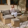 A woman is sitting on a rattan sofa set outdoors, holding a cup of coffee. Produktbild-Vorschau