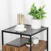 A close-up view of a modern side table with a glass top, a drawer, and shelves, decorated with a plant, a cup and saucer, and a decorative candle holder. Produktbild-Vorschau