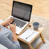 A person using a laptop on a lap desk while sitting on a couch. Produktbild-Vorschau
