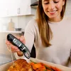A woman is using a digital food thermometer to check the temperature of a cooked piece of meat in a roasting pan with vegetables. Anteprima dell’immagine prodotto
