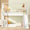 A white bunk bed with a slide and ladder, decorated with pillows and a hanging monkey toy. Produktbild-Vorschau