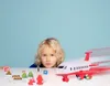 A young boy looks at toy airport accessories and a toy airplane on a white table. Produktbild-Vorschau