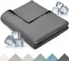 A folded dark gray blanket with a waffle texture is shown on a white background, with ice cubes scattered around it to suggest a cooling effect. Below the blanket, swatches of different colored blankets are visible. Anteprima dell’immagine prodotto