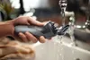 A hand is rinsing a Philips S 1142/00 electric shaver under running water in a sink. Podgląd zdjęcia produktu