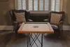 Two leather armchairs flank a wooden table with a carrom board on it, in front of a window with white shutters. Náhled obrázku produktu