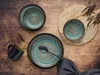 A rustic table setting with stoneware plates, bowls, a mug, and cutlery, accented by dried plant sprigs. Náhľad obrázku produktu