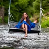 A woman sits on a swing over a river, wearing a blue dress. Podgląd zdjęcia produktu