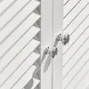 A close-up view of two silver cabinet knobs on a white louvered door. Produktbild-Vorschau