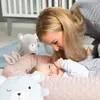A mother interacting with her baby in a nursery setting, surrounded by plush toys. Produktbild-Vorschau