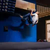 Ein Kletterer trainiert an einem VerticalBoard One von YY Vertical; umgeben von Klettergriffen und einer blauen Wand. Produktbild-Vorschau