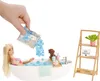 A Barbie doll is taking a bath with blue bath confetti, a small dog, and bath accessories. A shelf with a plant and a sign that says "LOVE YOURSELF" is in the background. Náhľad obrázku produktu