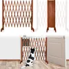 A wooden expandable gate is set up in a doorway, with a dog sitting in front of it. Produktbild-Vorschau