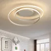A modern LED ceiling light fixture with a swirling design, installed on a white ceiling in a room with patterned wallpaper and framed artwork. Produktbild-Vorschau