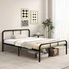 A black metal bed frame is set up in a bedroom with decorative wall art and plants. Voir les images du produit