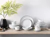 A collection of white porcelain dinnerware with black trim, arranged on a wooden surface with a green fern in a black vase. Podgląd zdjęcia produktu