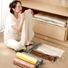 A woman is sitting on the floor in front of an open closet, holding a cream-colored sweater. Several rolled-up vacuum storage bags in different colors are laid out on the floor in the foreground. Voir les images du produit