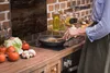 A person is cooking in a kitchen, with vegetables and cooking utensils visible on the countertop. Produktbild-Vorschau