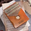 A wooden kalimba rests on sheets of music, with glasses in the background. Produktbild-Vorschau