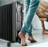 A person's legs and feet are shown next to a black oil-filled radiator heater. Anteprima dell’immagine prodotto