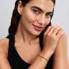 A woman wearing a black top and a gold bracelet with a charm. Náhled obrázku produktu