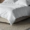 A close-up view of a bed with grey and white patterned bedding. Produktbild-Vorschau