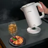 A person is pouring hot water from a white electric kettle into a glass of tea, with a croissant and raspberries on a plate nearby. Produktbild-Vorschau