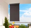 A balcony with a roller blind partially covering the view of the sky and buildings. A table with drinks and a plant are in the foreground. Produktbild-Vorschau
