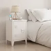 A white bedside table with a lamp, a framed picture, and a cup of coffee on top, next to a bed with white bedding. Voir les images du produit