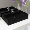 Two black ceramic sinks with chrome faucets are shown on a white countertop, with a tiled wall and a vase of purple flowers in the background. Produktbild-Vorschau
