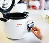 A hand is shown adjusting a dial on a white Tefal Cook4me+ smart multi-cooker, with the lid open. Podgląd zdjęcia produktu