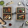 A tabletop grill with food being cooked on it, set on a grey surface with various food items and utensils around it. Produktbild-Vorschau