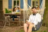 A man is relaxing in a hammock chair outdoors, with a family in the background. Náhled obrázku produktu