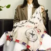 A person sitting on a couch holding a blanket with a vintage airmail design. Produktbild-Vorschau