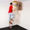 A man is climbing a retractable attic ladder into an opening in the ceiling. Produktbild-Vorschau