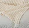 A close-up view of a soft, cream-colored blanket with a ribbed texture, draped over a white surface, likely a bed or sofa. Podgląd zdjęcia produktu