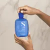 Hands holding a blue bottle of shampoo against a marble-like background. Anteprima dell’immagine prodotto