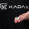 A hand holds small white plastic components in front of a black t-shirt with a logo. Voir les images du produit