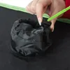 A hand is shown pulling a green drawstring on a black fabric pouch attached to a larger black surface with a green trim. Náhled obrázku produktu