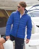 A man wearing a blue puffer jacket and navy shorts stands on a boat. Produktbild-Vorschau