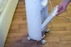 A hand is shown pulling out a filter from a white air cooler on a wooden floor. Náhled obrázku produktu