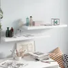 Two white floating shelves mounted on a light blue wall, decorated with various items including bottles, a box, a decorative cube with a butterfly, a framed artwork, and a stack of magazines on a white table. Náhľad obrázku produktu