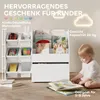 A white children's bookshelf filled with books and toys, with a baby sitting on the floor in front of it, looking at an open book. Produktbild-Vorschau