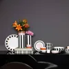 A collection of Villeroy & Boch Memphis tableware and vases with flowers, displayed on a black surface against a gray background. Voir les images du produit