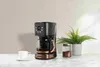 A black and copper coffee maker is displayed on a marble countertop next to a white coffee cup and a jar of coffee grounds. Náhled obrázku produktu