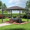 A gazebo with a hardtop roof is set up in a backyard garden, with a hot tub placed on a wooden deck underneath. Lush green grass, hedges, and flowering bushes surround the scene. Produktbild-Vorschau