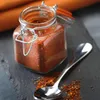 A close-up shot of a small glass jar filled with spices, with a spoon and spilled spices on a dark slate surface. Anteprima dell’immagine prodotto