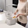 A woman is adding food waste to a compost bin in a kitchen. Voir les images du produit