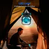 A person sitting inside a tent at sunset, with a portable fan and light hanging above. Produktbild-Vorschau